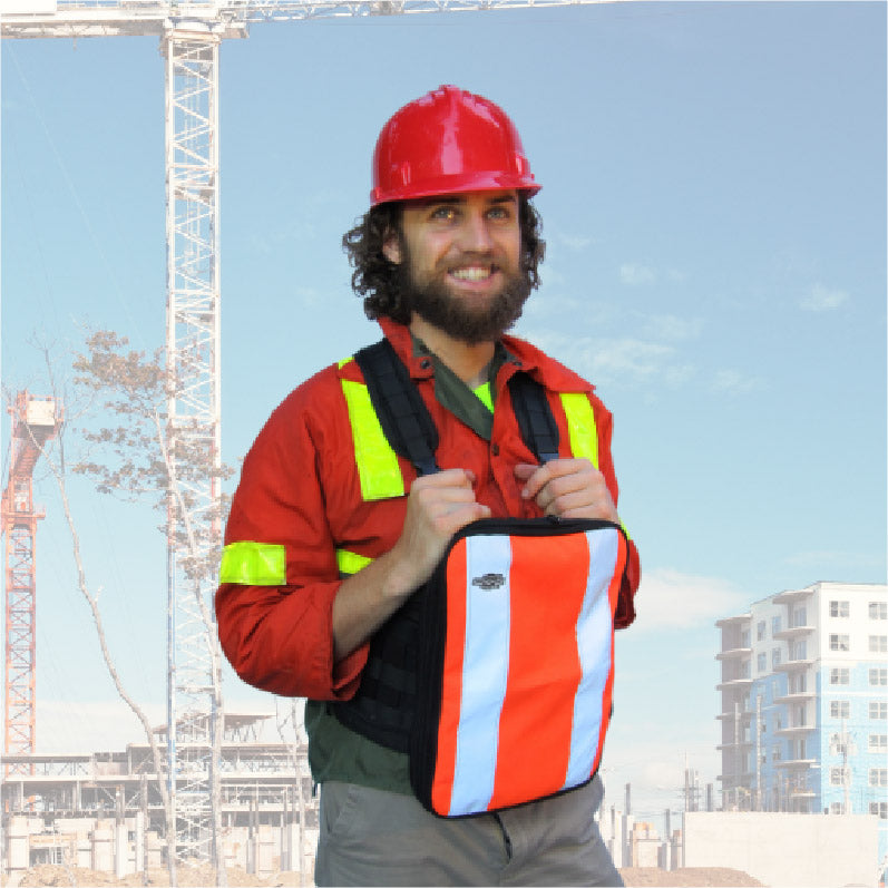 Smiling construction worker wearing a red hard hat and high-visibility clothing, demonstrating the Fitek Ruxton Chest Pack with a high-visibility orange and reflective tablet pack standing in front of a construction site.